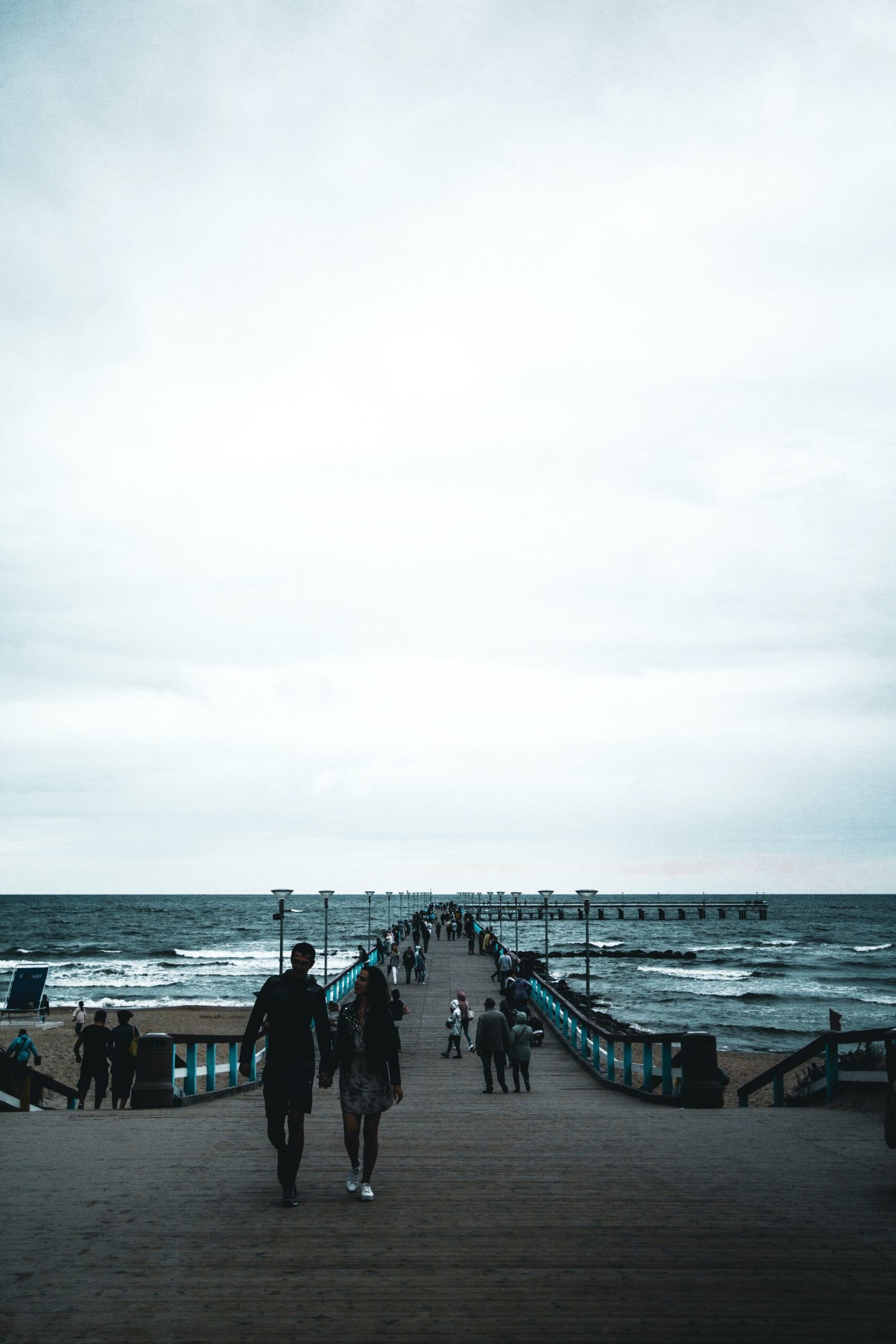 a group of people walking down a pier next to the ocean