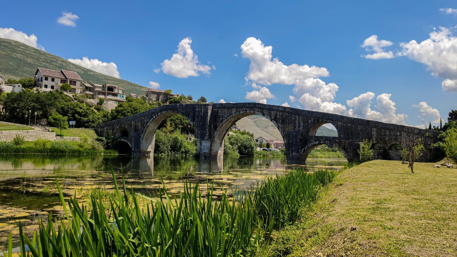 a stone bridge over a river with a person walking on the side