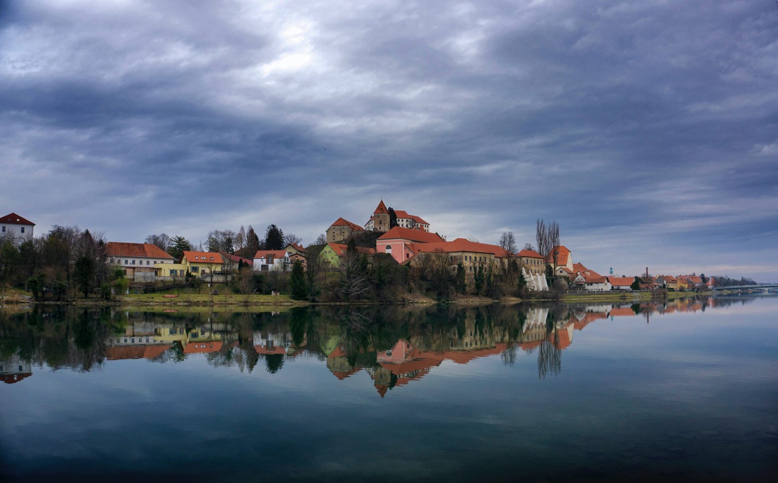 brown and white concrete house near body of water under gray clouds