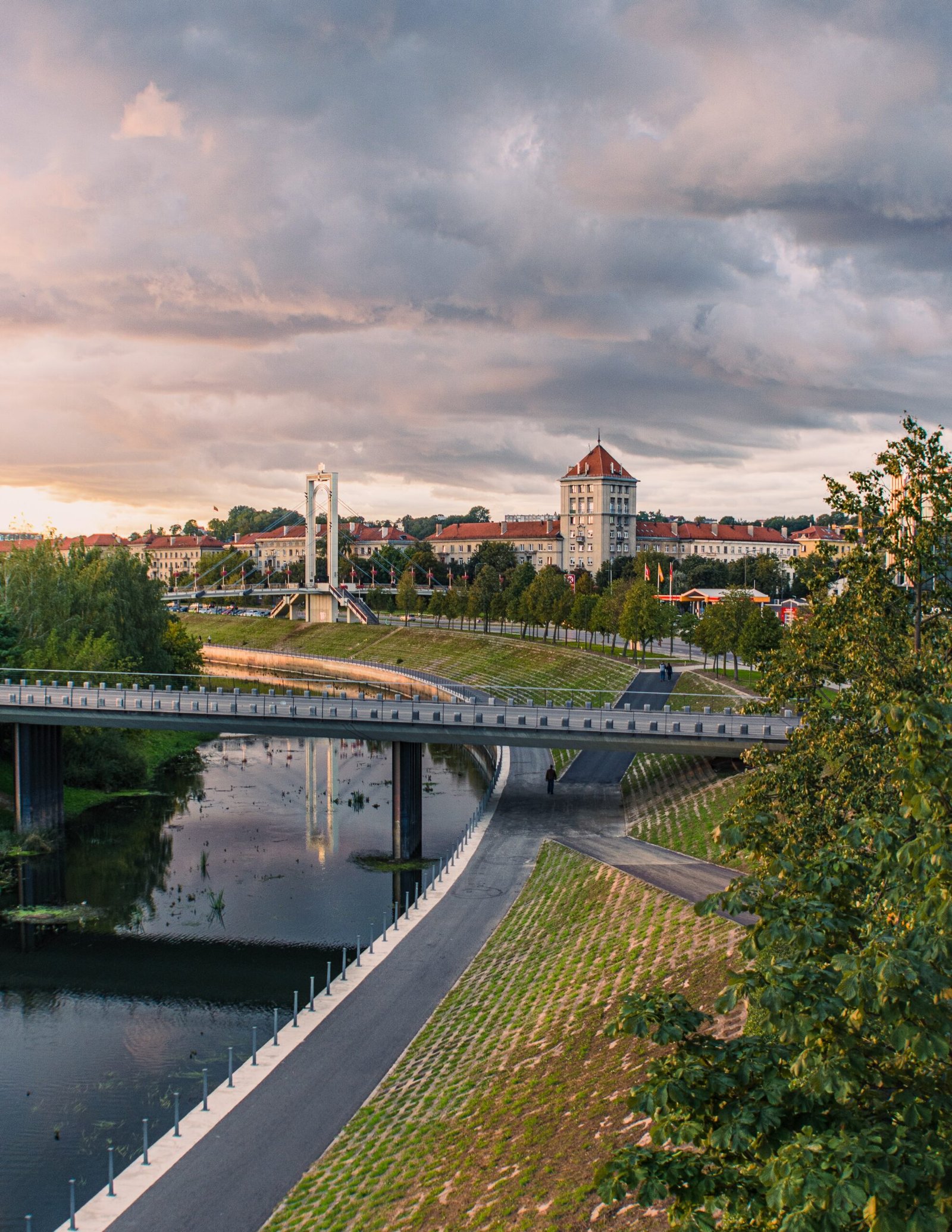 brown concrete building near green trees and river under cloudy sky during daytime