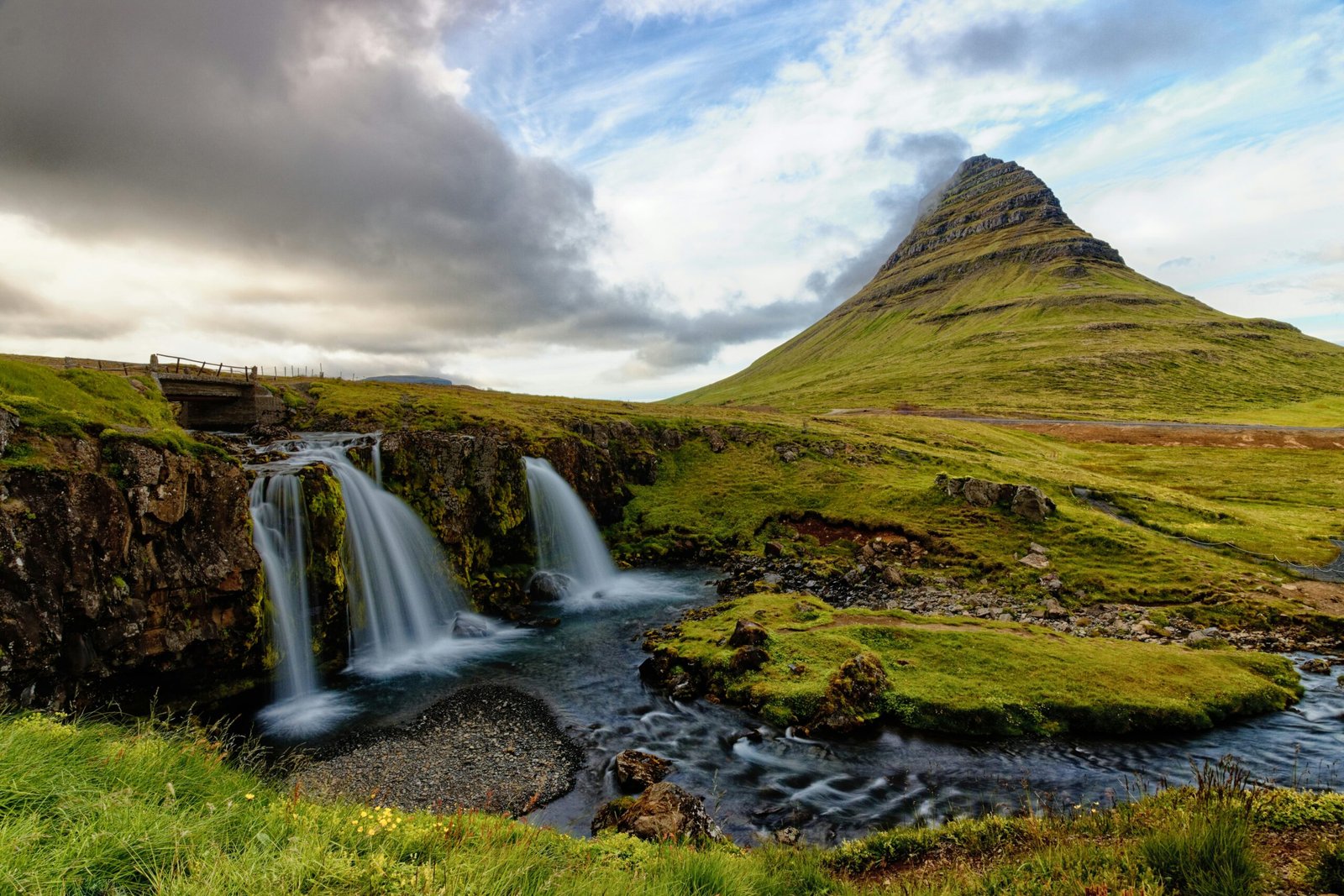 green grass field near waterfalls under cloudy sky during daytime