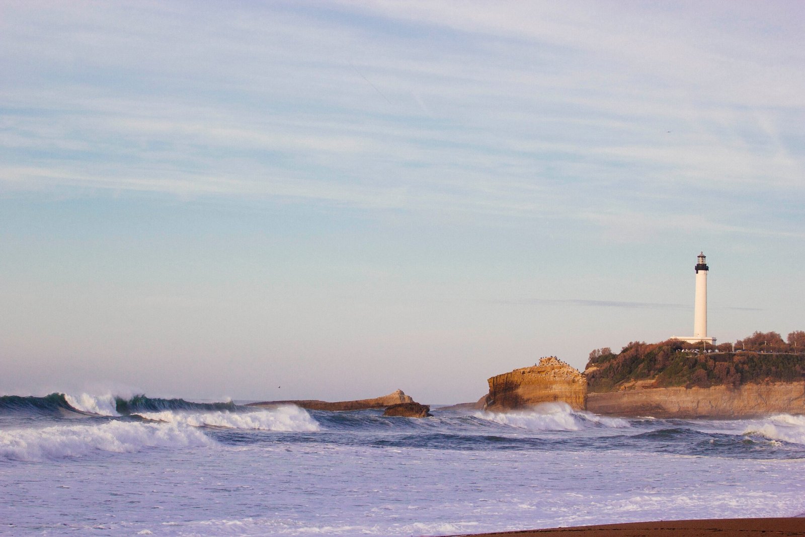 lighthouse on hill near ocean under blue sky at daytime