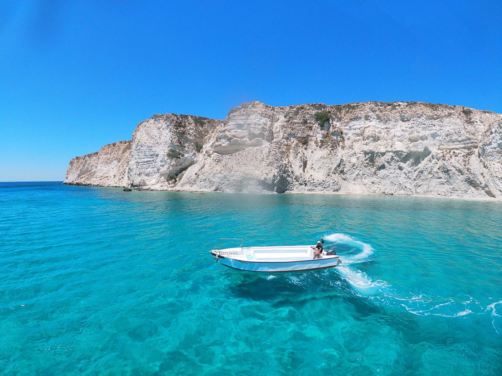 white and blue boat on blue sea near gray rocky mountain during daytime